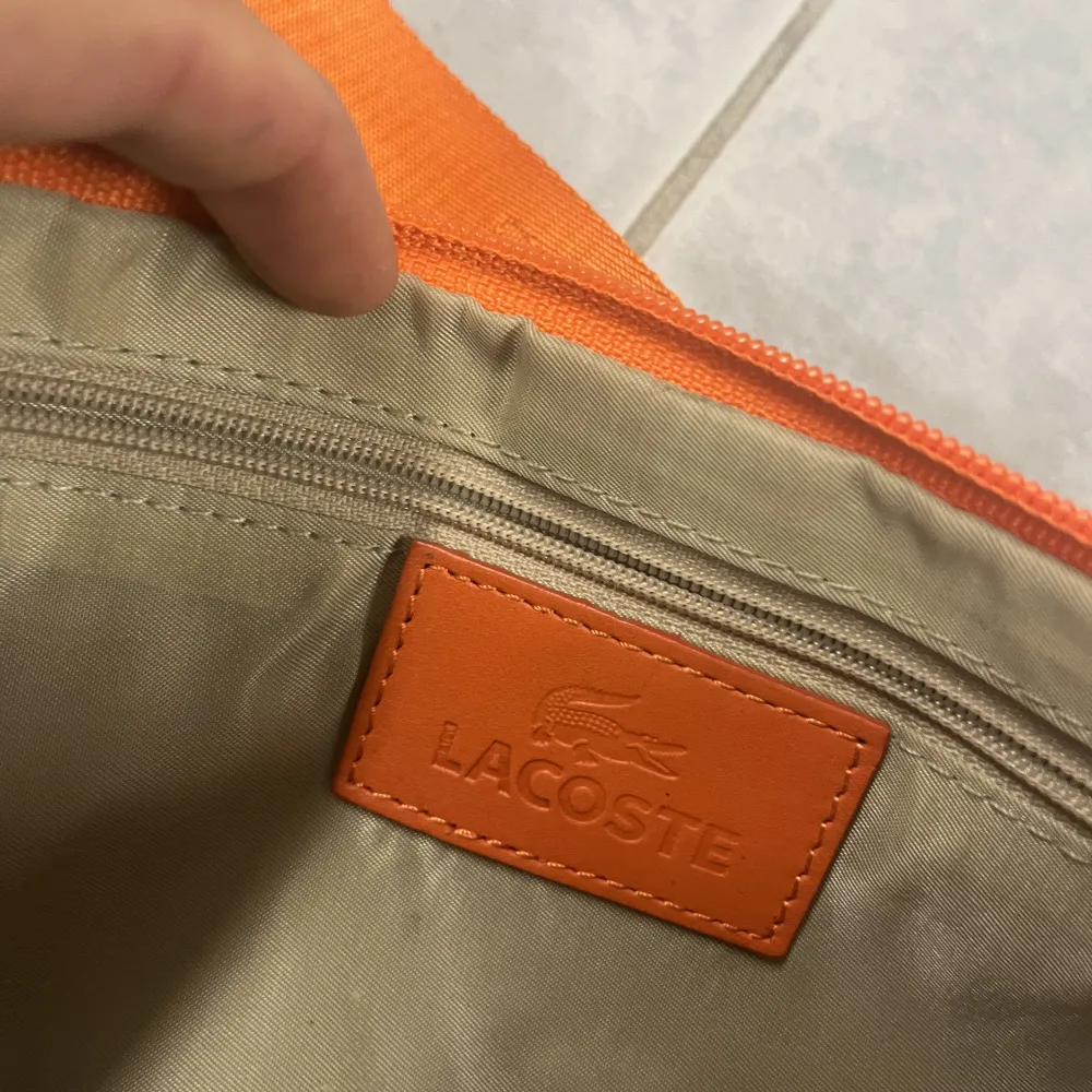 Orange väska från Lacoste i nyskick, ingenting att anmärka på. Accessoarer.