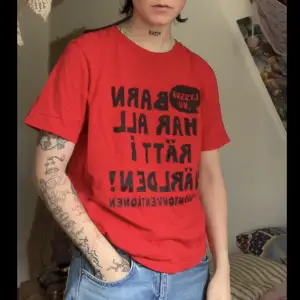 En röd T-shirt med citat ur barnkonventionen, aldrig använd 