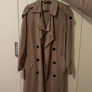 Trenchcoat  - Lång trenchcoat med bälte. Oanvänd 