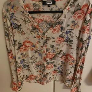 Blommig skjorta från Bik Bok, S - Superfin blommig skjorta från Bik Bok i ljusa färger med rosa, blå och gula blommor. Skjortan har v-ringning, knappar framtill och långa ärmar. 