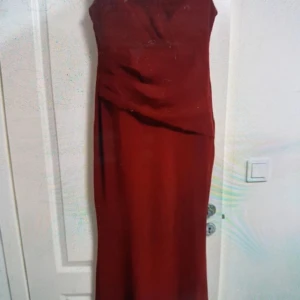 Vinröd långklänning med omlott - Snygg vinröd långklänning med omlott-detalj över bysten och markerad midja. Ärmlös modell med dragkedja i ryggen. Perfekt för dig som vill sticka ut med en elegant och stilren look.