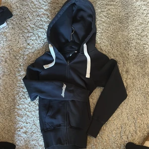 Blå hoodie från RusseMerch - Mörkblå russemerch hoodie med dragkedja, den är lite tajt i midjan men annars väldigt fin!