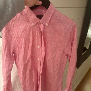 Rosa linneskjorta Oscar Jacobson M - Snygg rosa skjorta från Oscar Jacobson i storlek M med smal passform. Skjortan är tillverkad i linne, har klassisk krage med knappar och långa ärmar. Perfekt för dig som gillar stilrena och fräscha plagg med en modern touch.
