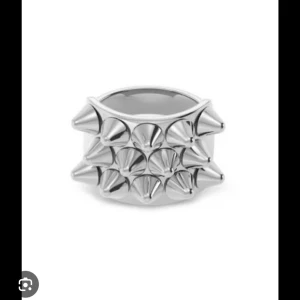 Bred silverring med nitar - Cool bred ring i silverfärg med flera spetsiga nitar runt hela ringen. Perfekt statement piece för dig som gillar edgy och unik stil. Ringen har en blank finish och känns riktigt tung och robust. Säljer virala Edblad ringen då den inte kommer till användning längre❤️