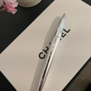 Benefit Mighty Fine Brow Pen 5 - Snygg ögonbrynspenna från Benefit i färgen 5 Warm Black-Brown. Pennan har en smal spets för exakt applicering och kommer i en stilren, silvrig hylsa. Perfekt för att skapa naturliga och definierade bryn.