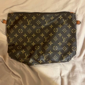  kuvertväska -  kuvertväska klassiskt monogrammönster. Väskan är brun blommor, tillverkad i skinn med dragkedja upptill och detaljer i läder. Perfekt för dig som vill ha en ikonisk accessoar med lyxig känsla.