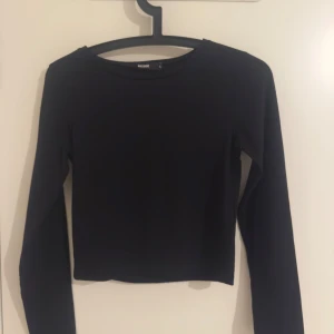 Svart croppad långärmad topp Bik Bok - En stilren svart croppad topp från Bik Bok med långa ärmar och rund halsringning. Enkel och snygg design som passar perfekt till jeans eller kjol. Gjord i mjukt material för en bekväm känsla.
