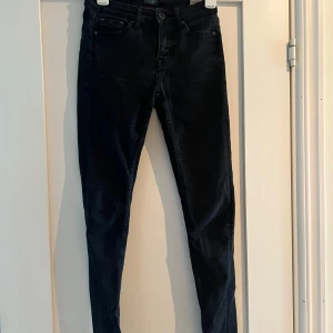 Svarta Crocker skinny jeans 25/30 - Svarta skinny jeans från Crocker, modell 211. Hög midja och super slim fit med klassiska fem fickor och orange söm på insidan. Jeansen är i stretchigt denim och har knapp och dragkedja 
