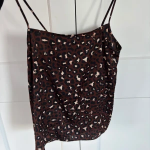 Leopardmönstrad brun kort klänning - Säljer en snygg kort klänning med leopardmönster i bruna och svarta toner. Klänningen har tunna axelband och ärmlös design, perfekt för dig som gillar att sticka ut. Materialet känns lätt och följsamt mot kroppen.