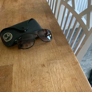 Ray-Ban solglasögon - Snygga Ray-Ban solglasögon med brunmelerad båge och rektangulär form. Glasen är tonade i brunt och bågen har en klassisk Ray-Ban-logga på sidan. Kommer med original svart fodral, putsduk och box. Perfekt för soliga dagar!