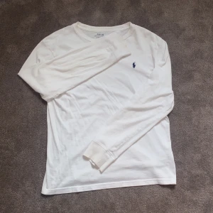 Vit långärmad tröja från Polo Ralph Lauren - Vit långärmad tröja från Polo Ralph Lauren med klassisk rund hals och den ikoniska broderade loggan på bröstet. Tröjan är gjord i mjuk bomull och har en clean och stilren look.  Nypris ca. 1000kr, mitt pris 299. Priset är prutbart. Hör av dig vid minsta funderingar så svarar jag direkt!