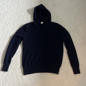 Mörkblå kashmirhoodie från Sayless - Mysig mörkblå hoodie från Sayless i lyxig kashmir. Klassisk modell med huva och dragsko, samt långa ärmar och ribbade muddar. Perfekt för dig som vill ha en stilren och skön tröja med premiumkänsla.