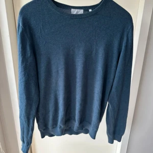 Blå stickad tröja från Bläck (prisförslag) - En stilren blå stickad tröja från Bläck i storlek L. Tröjan har rund halsringning, ribbade muddar och är långärmad. Perfekt för lager-på-lager och enkel att matcha med jeans eller chinos.