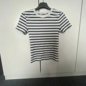 Randig t-shirt från Zara, vit och svart - Snygg t-shirt från Zara i vitt med svarta horisontella ränder. Klassisk rund halsringning och korta ärmar. Skön passform och tillverkad i mjuk bomull, perfekt till jeans eller kjol.