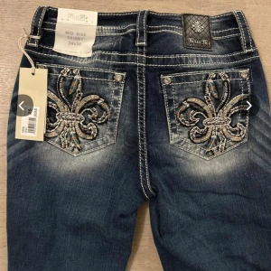 Miss Me skinny jeans med broderi köpta från LA - Snygga blå skinny jeans från Miss Me med broderade detaljer på bakfickorna och kontrastsömmar. Jeansen har midwaist passform och coolt sliten tvätt. Perfekta för dig som vill sticka ut med unika detaljer och bekväm passform.