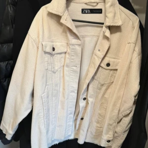 Beige manchesterjacka från Zara - Snygg beige manchesterjacka från Zara med klassisk krage och knäppning framtill. Jackan har två bröstfickor med lock och knappar samt raka sidfickor. Perfekt oversized passform och coola detaljer i manchestertyg.