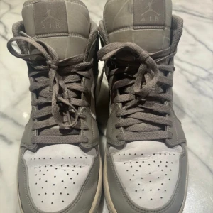 Nike Air Jordan 1 Mid grå/vit - Säljer ett par Nike Air Jordan 1 Mid i grått och vitt. Skorna har klassisk snörning, perforerad tåbox och ikoniska Air Jordan-loggan på sidan. Har lite märken men syns på bilen. Skriv för vidare frågor!