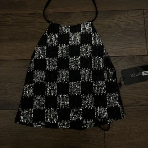 Svart och silver paljett-topp - Supersnygg halterneck topp från New Yorker i svart och silver med rutigt paljettmönster. Toppen har smala band i nacken och är croppad med en glittrig finish som verkligen sticker ut. Perfekt för dig som vill ha något extra till din outfit.