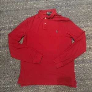 Röd långärmad pikétröja Ralph Lauren - Röd långärmad pikétröja från Polo Ralph Lauren i slim fit. Klassisk krage med två knappar och broderad logga på bröstet. Tillverkad i mjuk bomull, perfekt för en clean och stilren look.