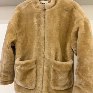 Beige teddyjacka från NA-KD - Mysig beige teddyjacka från NA-KD med rund krage och två stora fickor framtill. Perfekt för att hålla sig varm och snygg under kyliga dagar. Jackan är inte använd många gånger men har dessvärre har ena fickan lossnat lite i sömmen, vilket man knappt ser eller påverkas av. Se sista bilden så förstår ni!