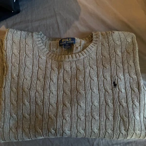 Ralph Lauren stickad grå - Kabelstickad grå tröja från Polo Ralph Lauren i storlek XL. Klassisk rund halsringning, långärmad och med broderad logga på bröstet. Tröjan är stickad i bomull och har ribbade muddar vid ärmslut och nederkant. Perfekt för höst och vinter. Mannen på bilden är 182cm o väger ca 73kg (tröjan har passform som en Medium herr) Nypris 2400kr. För mer frågor, skriv privat!    Först till kvarn