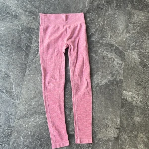 Rosa seamless leggings  - Säljer ett par rosa seamless leggings med hög midja och ribbade detaljer längs benen. De är stretchiga och sitter tight, perfekta för träning eller chill. Materialet är mjukt och följsamt, och färgen är en snygg ljusrosa nyans.