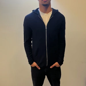 Mörkblå cardigan/kofta från Ljung Marcus Larsson - Säljer en mörkblå cardigan från Ljung by Marcus Larsson i storlek M. Tröjan har dragkedja framtill, huva och två fickor. Enkel och stilren design som passar perfekt till jeans eller joggers. NYPRIS:1899Kr Mitt pris:499Kr