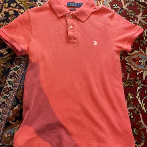 Korallrosa pikétröja från Polo Ralph Lauren - Säljer en rosa pikétröja från Polo Ralph Lauren i slim fit-modell. Tröjan har klassisk krage, korta ärmar och två knappar framtill. Pikén är äkta från Ralph Lauren och passar en person som är 165-170 cm lång men är egentligen storlek 152 men pikén passar mig och jag är 170 cm lång. Diskutera pris om nödvändigt/vill😊👔