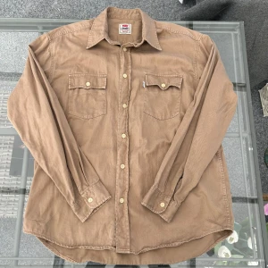 Min Levi’s vintage westernskjorta – strl L, brun/beige 100% bomull - Snygg vintage Levi’s westernskjorta i brun/beige ton. Klassisk modell med två bröstfickor, knappstängning och Levi’s logga på fickan. Tillverkad i 100% bomull – perfekt både som vardagsskjorta eller overshirt. Storlek L.  🪡 Skick: Mycket bra vintage skick, inga större slitningar eller defekter. Äkta Levi’s.  Passar både till jeans, chinos eller som lager-på-lager för en retro streetwear-look. 