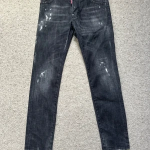 Svarta Dsquared2 Cool Guy Jean / slim - Säljer ett par svarta Dsquared2 Cool Guy jeans med slitna detaljer och snygg tvätt. Jeansen har fem fickor, smal passform och klassisk Dsquared2-lapp bak i midjan. Perfekta för dig som gillar en edgy streetstil.