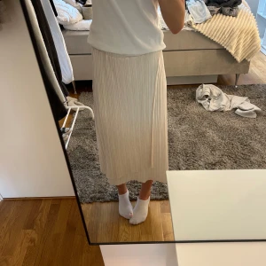 Plisserad beige långkjol - Säljer en snygg plisserad långkjol i ljus beige färg. Kjolen har en rak och flowy siluett med elastisk midja som gör den bekväm att bära. Perfekt för dig som gillar stilrena och enkla plagg med lite extra detalj tack vare de fina plisseringarna.