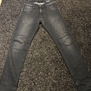 Replay svarta slim jeans W30/32 - Säljer ett par svarta Replay jeans med diskret tvättad look. Modellen är slim fit med klassiska fem fickor och snygga detaljer på bakfickorna. Jeansen har normal midja och är tillverkade i stretchigt denim för en bekväm passform.