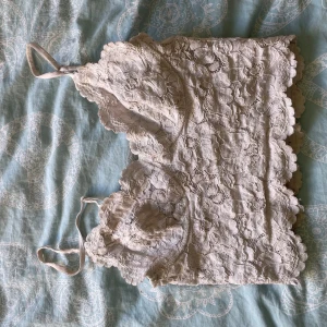 Vit spetsig linnetopp från Amisu - Supersöt vit linnetopp från Amisu i storlek XS. Toppen har tunna axelband och är helt täckt av blommig spets med vågiga kanter. Perfekt för dig som gillar romantisk och feminin stil. Fodrad på insidan för extra komfort.