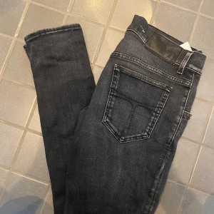 Svarta slim jeans från Tiger of Sweden - Säljer ett par svarta slim jeans från Tiger of Sweden med klassiska bakfickor och diskreta slitningar. Jeansen har en smal passform och är tillverkade i stretchigt denim för extra komfort. Perfekta för dig som gillar en skön look och vill ha ett par stilrena jeans.