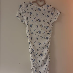 Vit blommig klänning storlek 158 (åldrar 12-13) - Supersöt vit klänning från Shein Teen med blå blommor och korta ärmar. Klänningen har en ribbad struktur, snörningsdetalj i sidan och är figurnära. Perfekt för dig som gillar romantiska och fräscha vibes.