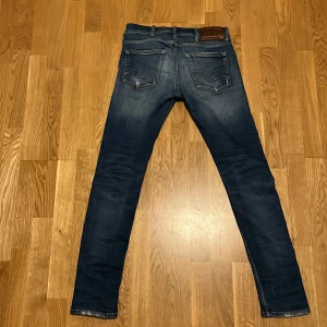 Replay Jondrill blå jeans slim fit - Säljer ett par Replay Jondrill jeans i mörkblå tvätt med snygga slitningar och klassiska fem fickor. Jeansen har smal passform, låg midja och detaljerade sömmar på bakfickorna. Perfekta för dig som gillar en modern och stilren look.