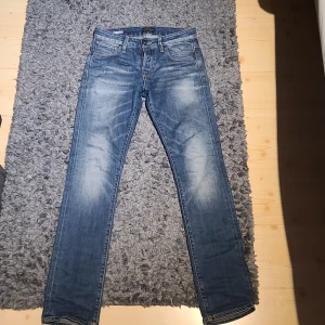Blå jeans från Jack & Jones - Snygga blå jeans från Jack & Jones med klassisk femficksdesign och läderpatch bak. Jeansen har en rak passform och är tillverkade i slitstarkt denimtyg. Perfekta för dig som gillar en tidlös och enkel stil.
