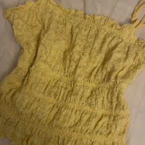 Gul spettröja från BikBok - Supersöt gul topp från BikBok med smala axelband och volangkant upptill. Toppen har broderade spetsdetaljer och smockad midja för en bekväm passform. Passar som S