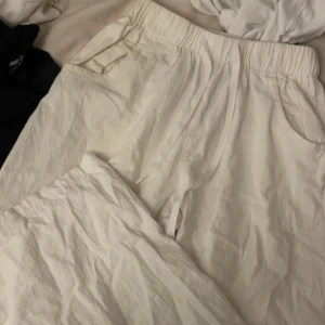 Vita linnebyxor med resår och snörning - Säljer ett par vita linnebyxor med avslappnad passform, resår i midjan och snörning framtill. Byxorna har sidfickor och är perfekta för en chill och luftig stil. Materialet är lätt och andas, vilket gör dem sköna att bära under varmare dagar. Storlek XS