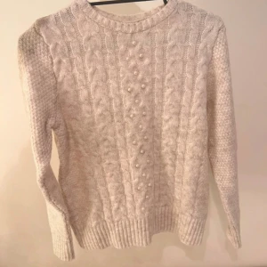 Beige stickad tröja med pärlor LC Waikiki - Superfin beige stickad tröja från LC Waikiki med flätstickat mönster och pärldetaljer framtill. Tröjan har rund halsringning, ribbade muddar och långa ärmar. Perfekt för dig som gillar en mysig och stilren look. Använd bara en gång!