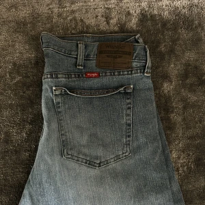 Blåa Wrangler jeans - Klassiska blå jeans från Wrangler med raka ben och femficksmodell. Jeansen har en ljus tvätt, normal passform och är tillverkade i slitstarkt bomullsjeans. Snygg detalj med Wrangler-lapp bak i midjan och röd etikett vid fickan.