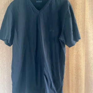 Svart v-ringad t-shirt från BOSS - Svart t-shirt från BOSS med v-ringning och diskret logga på bröstet. Klassisk passform och tillverkad i mjuk bomull. Perfekt för en clean och stilren look.