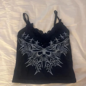 Svart linne med spets och tryck - Marinblått linne med tunna axelband och snygg spetskant vid urringningen. Framsidan har ett stort ljusblått tryck, Perfekt för dig som gillar detaljer och vill sticka ut. Materialet känns mjukt och följsamt. Priset går att diskuteras om! i bra skick💗