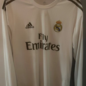 Real Madrid långärmad tröja - Bilden visar en vit långärmad Real Madrid-tröja från Adidas med Fly Emirates-tryck och Climachill-teknologi. 2019-2020 model.