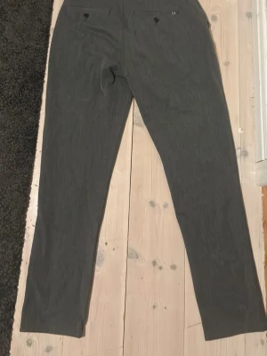 Grå kostymbyxor från Solid W29 L32 - Snygga grå kostymbyxor från Solid med rak passform och klassisk midja. Byxorna har knappstängning fram och bälteshällor. Materialet är mjukt och har en lätt struktur som ger en stilren look. Perfekta för dig som gillar en clean och enkel stil.