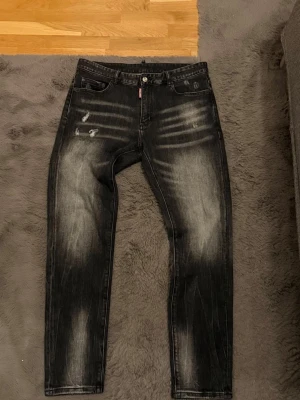 Svarta Dsquared2 jeans med slitningar - Säljer ett par svarta jeans från Dsquared2 i storlek 34. Jeansen har coola slitningar och blekta detaljer på både fram- och baksida, samt en patch med 'CIAO' på bakfickan. Slim fit-modell med klassisk femficksdesign, tillverkade i jeansmaterial. Använda vid 2 tillfällen. Priset kan diskuteras, hör gärna av dig vid frågor! 