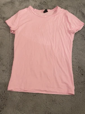 Ljusrosa t-shirt i bomull - Säljer en enkel och mjuk ljusrosa t-shirt med rund hals och korta ärmar. Perfekt för dig som gillar stilrena plagg och vill ha något bekvämt i garderoben. Materialet är bomull och modellen har en tight passform. Kan eventuellt tänka mig gå ner i pris