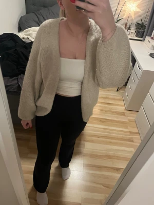 Beige stickad kofta från Lindex - Mysig och loose stickad kofta från Lindex i beige färg. Koftan har långärmade ärmar och öppen front utan knappar eller dragkedja. Perfekt att slänga på sig när det är lite kyligt ute. Passar dig som gillar en chill och enkel stil. Slutsåld på Lindex.