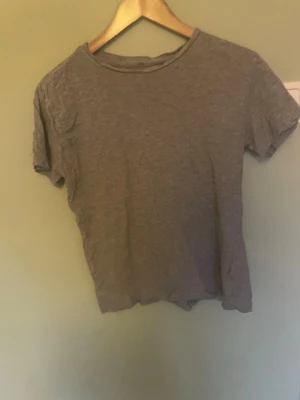 Grå basic t-shirt i bomull - En enkel grå t-shirt med rund hals och korta ärmar. T-shirten är tillverkad i mjuk bomull och har en klassisk passform som funkar till många olika stilar. Perfekt för dig som gillar en clean och avslappnad look.