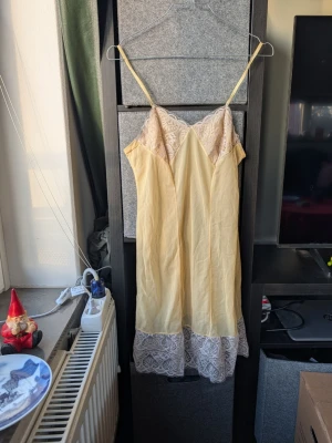 Ljusgul klänning med spetsdetaljer - Säljer en ljusgul kortklänning med tunna axelband och vackra spetsdetaljer i vitt vid byst och nederkant. 